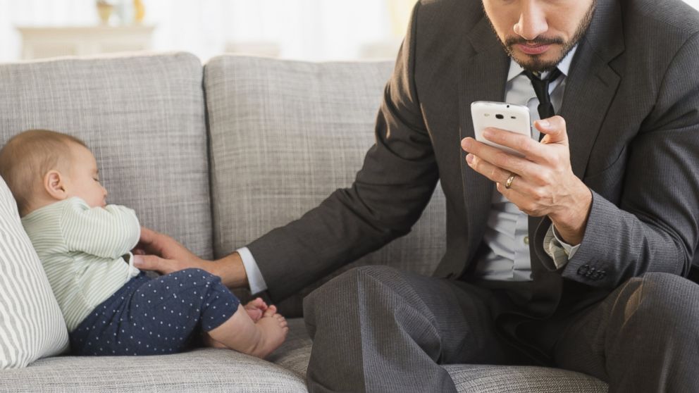 A father can be seen working while his child sleeps in this stock image.