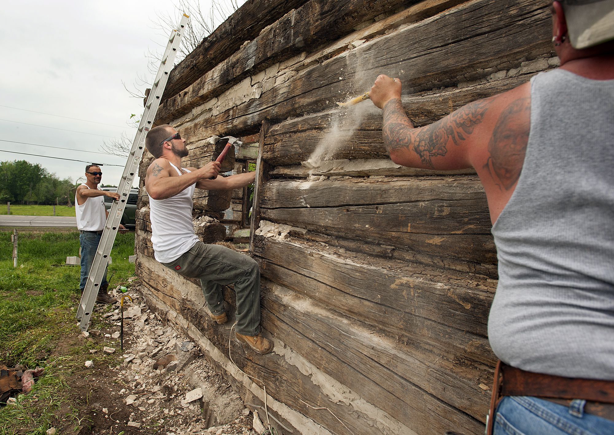 PHOTO: Jesse D. Martin, Madrid, and employee for D.D. Construction, clings to the side of a historic log cabin Wednesday that he and other coworkers were dismantling along route 68 in Lisbon.