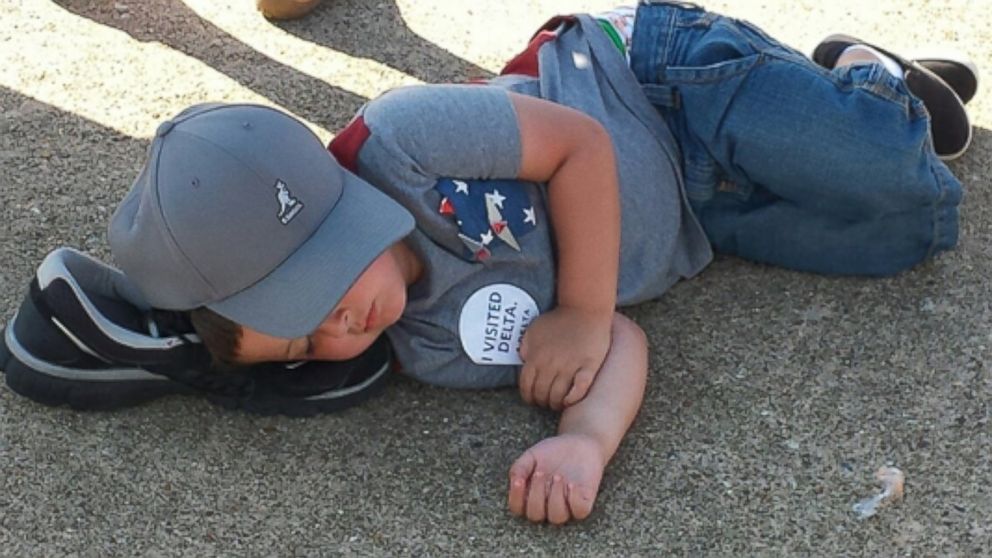 A boy is seen using a shoe as a pillow while sleeping on the ground at the NAS Oceana Air Show in Virginia Beach, Va.
