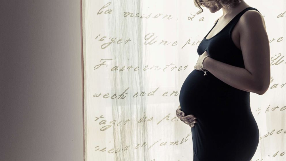 PHOTO: A pregnant woman holds her belly by a window in an undated stock photo.