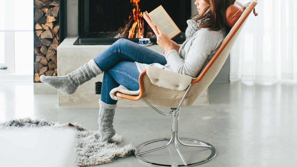 An undated stock photo of woman reading a book in front of fireplace in Sweden. 