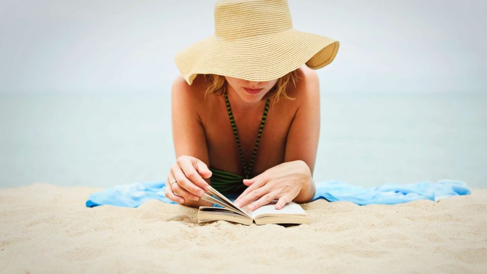 A young woman reads a book on the beach in an undated stock photo.