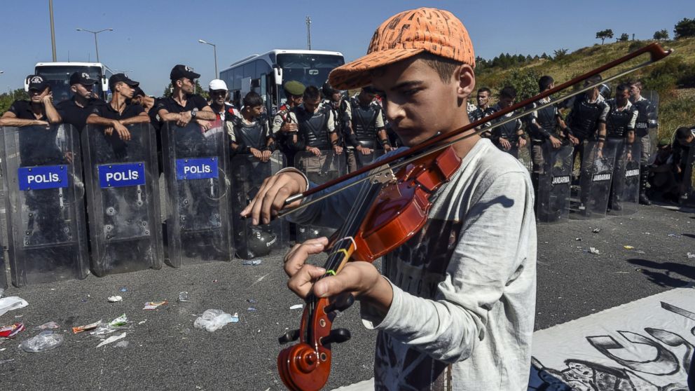 Alameddin, a 13-year-old Syrian boy, plays the violin in front of a police barricade as he marches toward the border between Turkey and Greece with other refugees, in Turkey, Sept. 19, 2015.