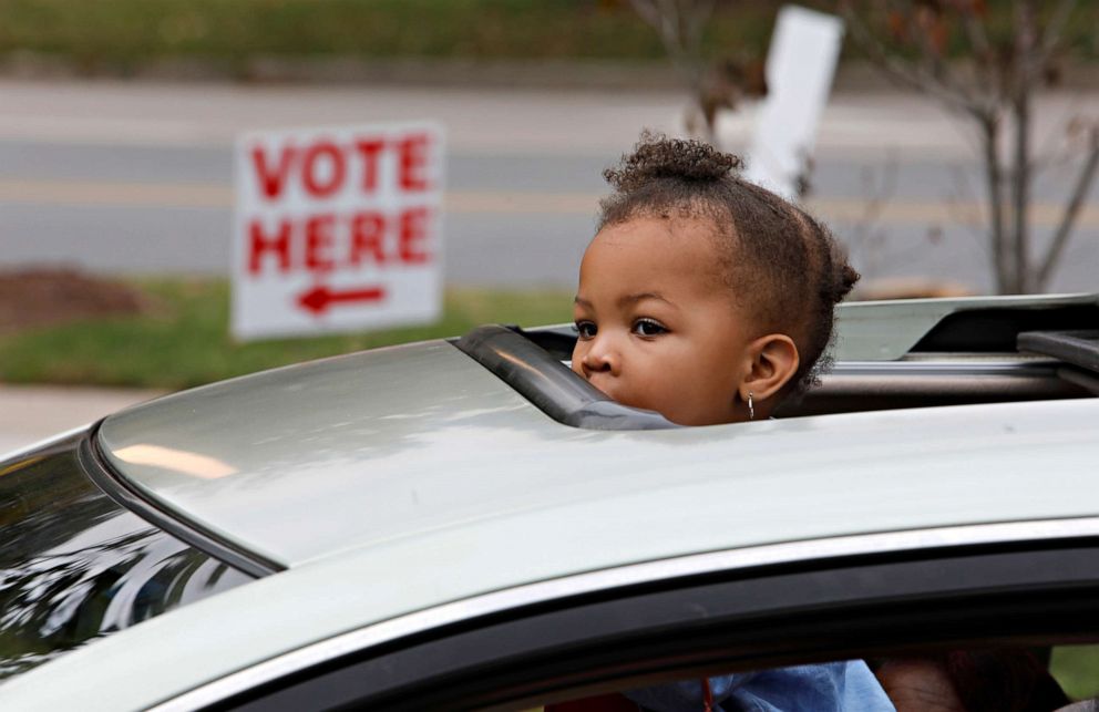 PHOTO: A child peers out from the sunroof of a car as its occupants wait in a line of vehicles for curbside voting on the first day of the state's in-person early voting for the general election at a polling place in Durham, N.C., Oct. 15, 2020.