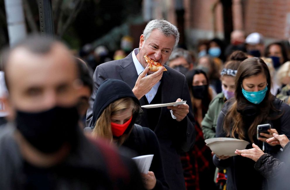 PHOTO: New York City Mayor Bill de Blasio eats pizza as he stands in line with hundreds of other voters for several hours to cast his ballot during early voting in Brooklyn, New York, Oct. 27, 2020.