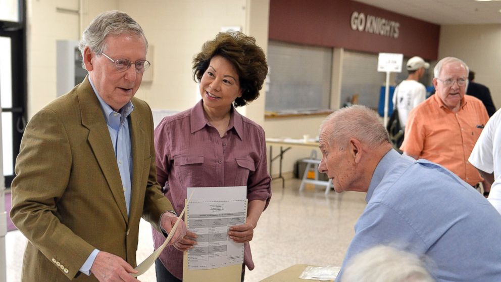 Kentucky Republican Senator Mitch McConnell, left, and his wife Elaine Chao, center, talk with poll workers as they sign in at their precinct, May 20, 2014, at Bellarmine University in Louisville, Ky.  