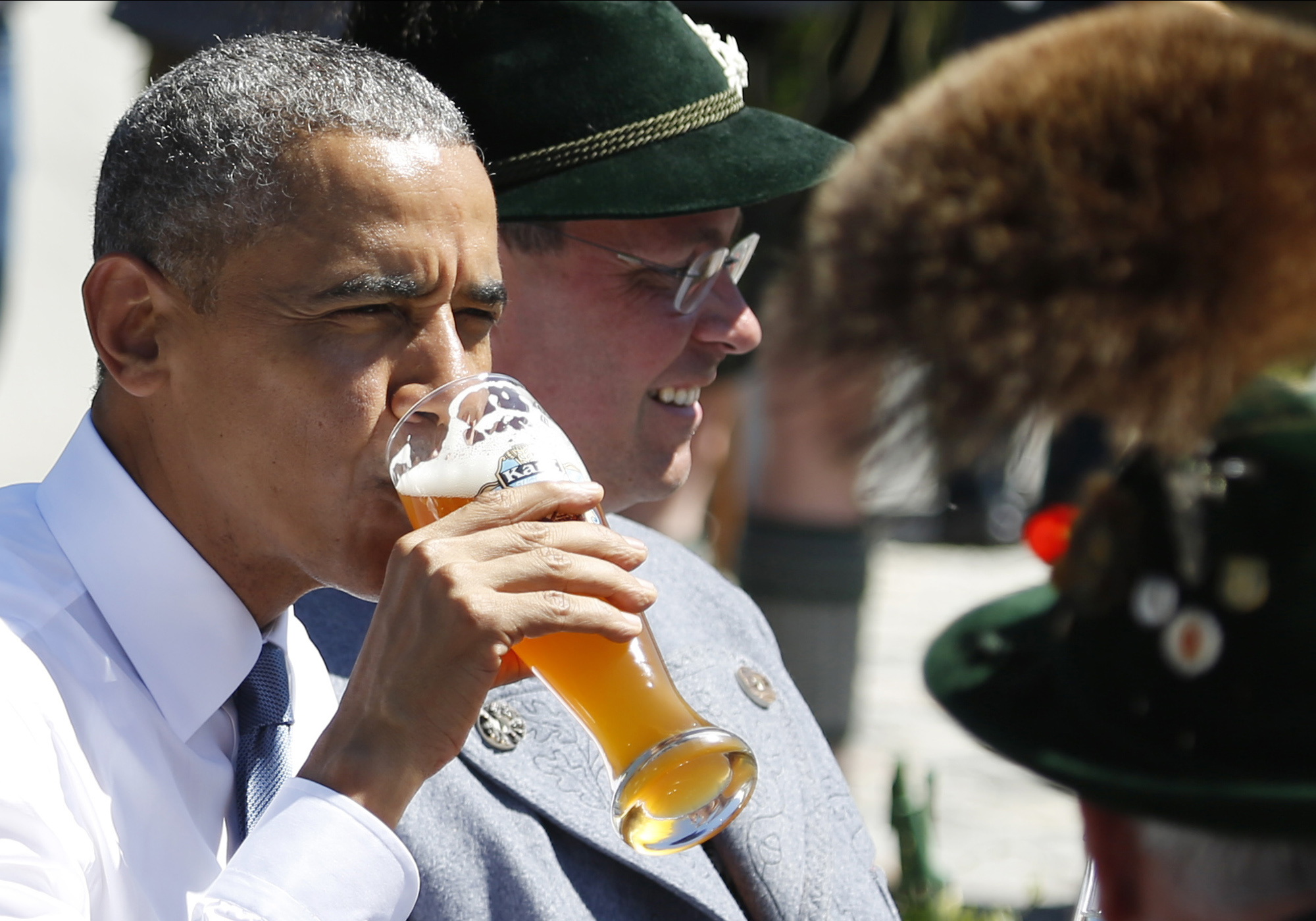 U.S. President Barack Obama drinks a beer as he sits between men dressed in traditional Bavarian clothes during a visit to the village of Kruen, southern Germany, Sunday, June 7, 2015 prior to the G-7 summit.