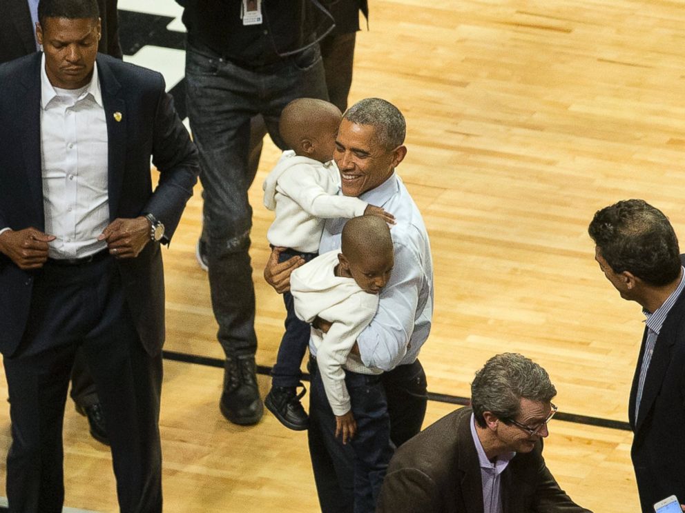 PHOTO: President Barack Obama carries two children as he poses for photos during halftime of a NBA basketball game between the Cleveland Cavaliers and the Chicago Bulls at the United Center in Chicago, Tuesday, Oct. 27, 2015.
