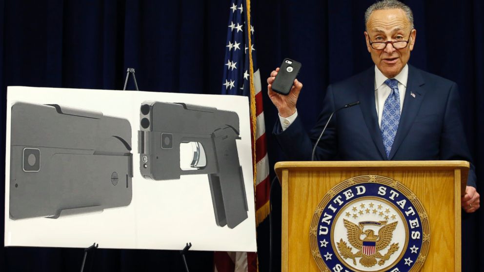 Standing beside photographs of a new product, Sen Charles Schumer shown holding an iPhone 5S, voices his opposition to a handgun that appears to be a cell phone during a news conference in his office, April 4, 2016, in New York.