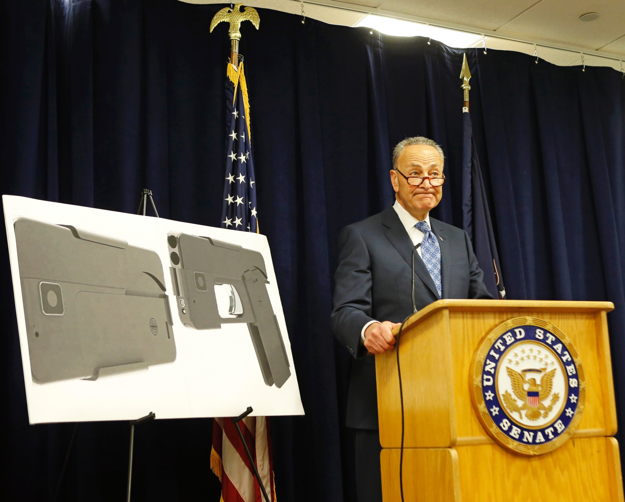 U.S. Sen Charles Schumer stands beside two photographs of what appears to be a cell phone, but is actually a handgun, during a press conference in his office,  April 4, 2016, in New York.  