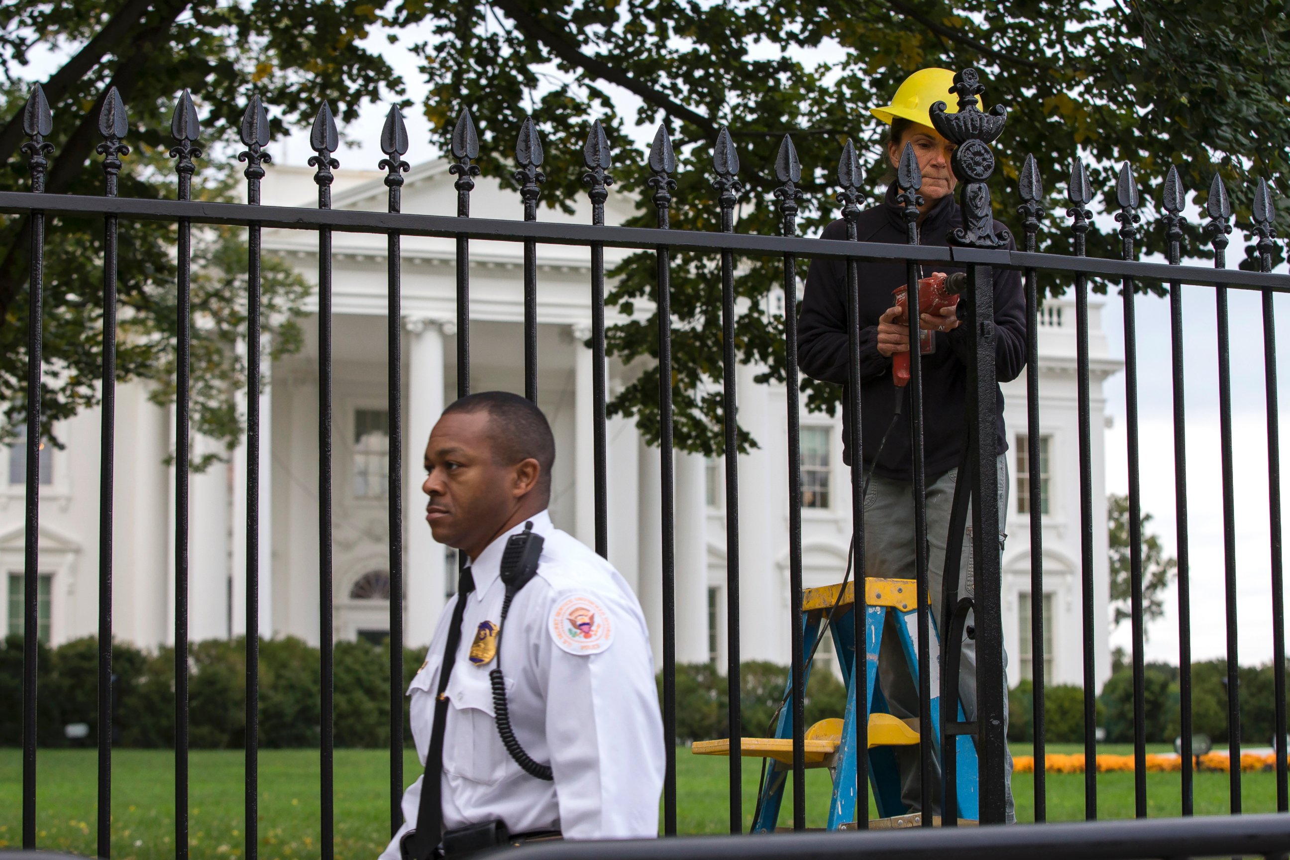 PHOTO: A Secret Service police officer walks outside the White House in Washington,  Oct. 23, 2014, as a maintenance worker performs fence repairs as part of a previous fence restoration project. 