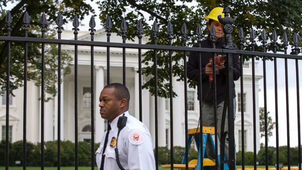 PHOTO: A Secret Service police officer walks outside the White House in Washington,  Oct. 23, 2014, as a maintenance worker performs fence repairs as part of a previous fence restoration project. 