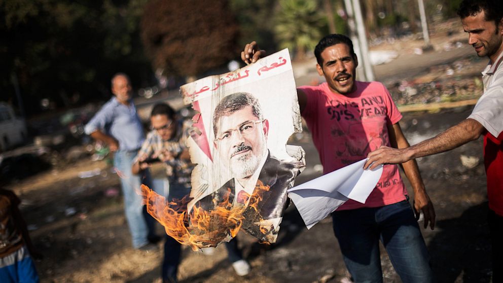 Egyptians against ousted President Mohammed Morsi burn his poster amid charred debris of the Nahda sit-in camp in Cairo, Egypt, Aug. 15, 2013.