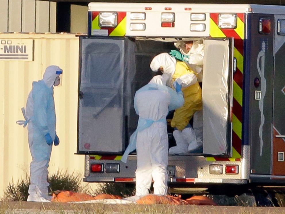 POTO: Medical staff in protective gear escort Nina Pham, exiting the ambulance, to a nearby aircraft at Love Field, Oct. 16, 2014, in Dallas.
