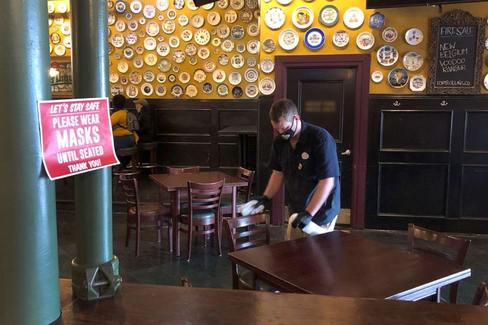 PHOTO: Cole Downing, a bartender, wears a protective mask as he cleans chairs and tables at the Flying Saucer Draught Emporium in Little Rock, Ark., May 11,2020.