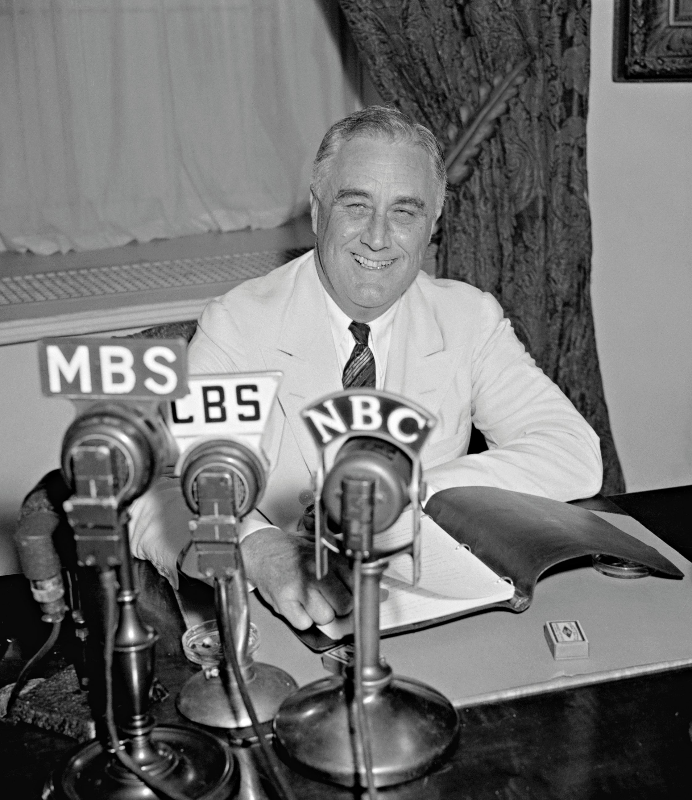 PHOTO: President Franklin D. Roosevelt smiles as he delivers one of his 'Fireside Chat' radio broadcasts from the Oval Office of the White House, Washington DC, 1938.