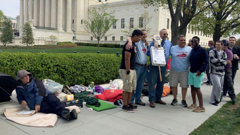 Kentucky same-sex supporters pose, as pastor Rick Grogan from Fort Worth, TX, an opponent, seated, looks on.