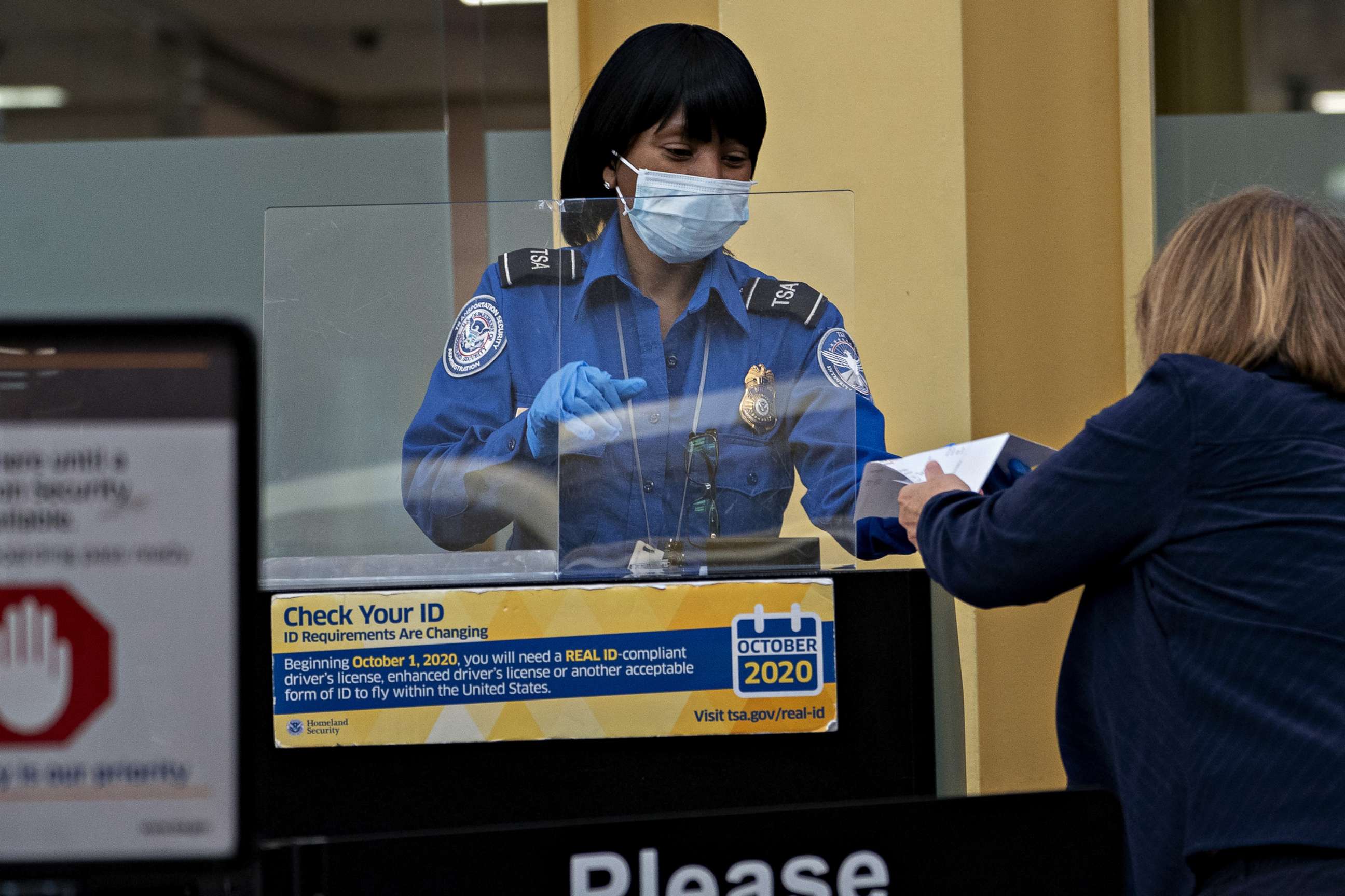 PHOTO: A Transportation Security Administration (TSA) agent wears a protective mask and stands behind a protective barrier while screening a traveler at Ronald Reagan National Airport (DCA) in Arlington, Va,, June 9, 2020. 