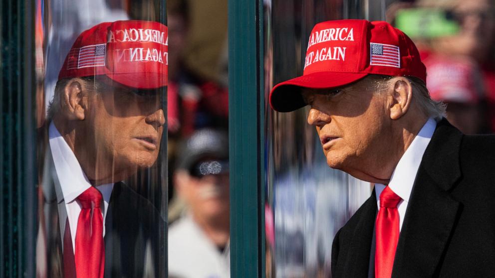 PHOTO:  Former US President Republican presidential candidate Donald Trump stands behind bulletproof glass as he arrives to speak during a campaign rally in Lititz, Pennsylvania, on November 3, 2024. 