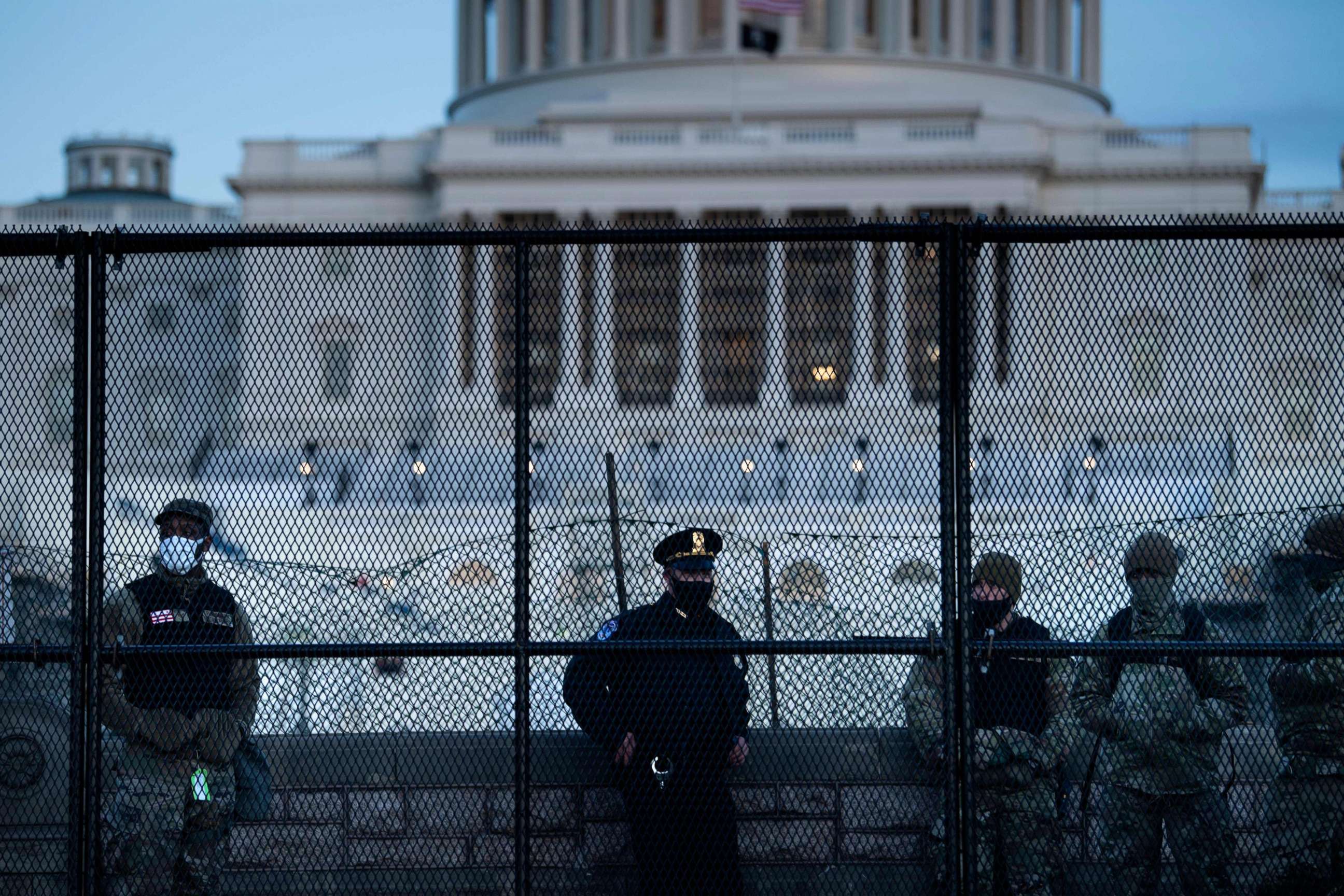PHOTO: TOPSHOT - A Capitol police officer stands with members of the National Guard behind a crowd control fence surrounding Capitol Hill a day after a pro-Trump mob broke into the US Capitol on Jan. 7, 2021, in Washington, D.C.