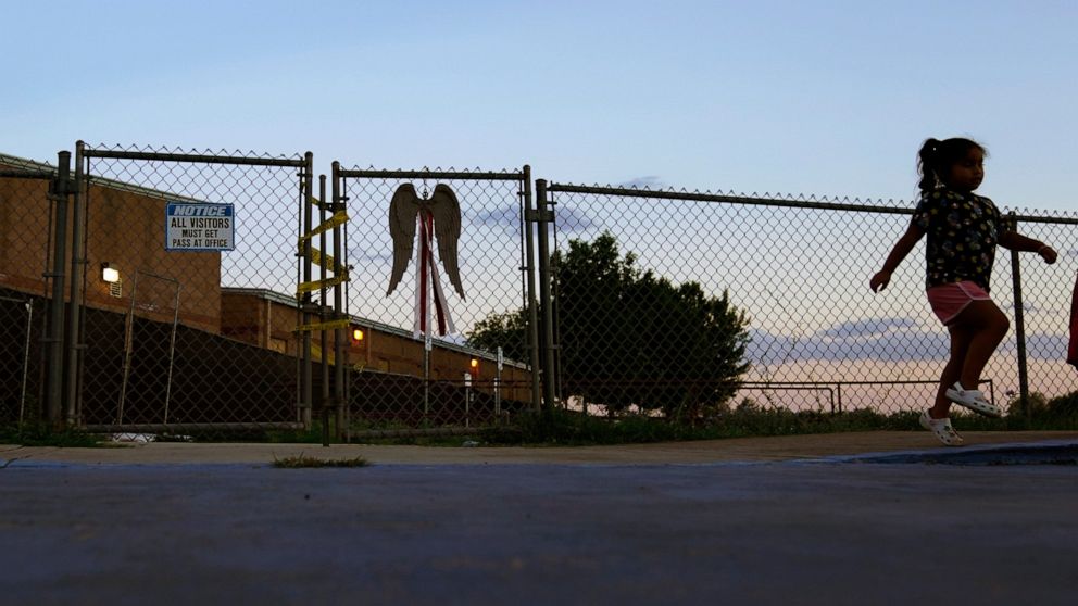 A girls skips past a gate at Robb Elementary School with police tape a locks, Sunday, July 10, 2022, in Uvalde, Texas. Students who survived the May 24 shooting at an elementary school in Uvalde, Texas are spending the summer grappling with post-trau