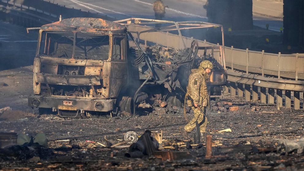A Ukrainian soldier walks past debris of a burning military truck, on a street in Kyiv, Ukraine, Saturday, Feb. 26, 2022. Russian troops stormed toward Ukraine's capital Saturday, and street fighting broke out as city officials urged residents to tak