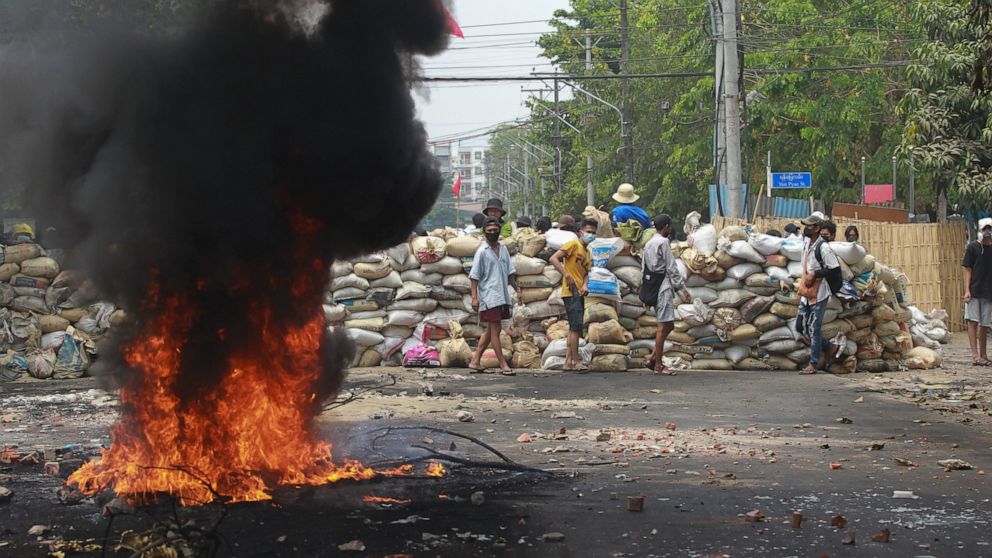 Anti-coup protesters stand beside a burning tire as they fortify their position against the military during a demonstration in Yangon, Myanmar on Tuesday March 30, 2021. Thailand’s prime minister denied Tuesday that his country’s security forces have
