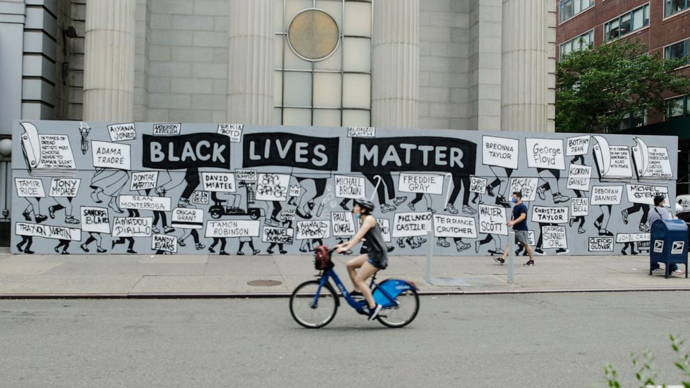 Pedestrians and a cyclist pass a mural in Union Square calling for justice over the death of George Floyd, and to highlight police brutality nationwide, Thursday, June 11, 2020, in New York. Floyd, a black man, died after he was restrained by Minneap