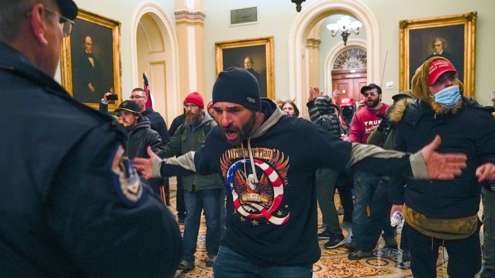 FILE - In this Jan. 6, 2021, file photo, Trump supporters gesture to U.S. Capitol Police in the hallway outside of the Senate chamber at the Capitol in Washington. Doug Jensen, an Iowa man at center, was jailed early Saturday, Jan. 9, 2021 on federal