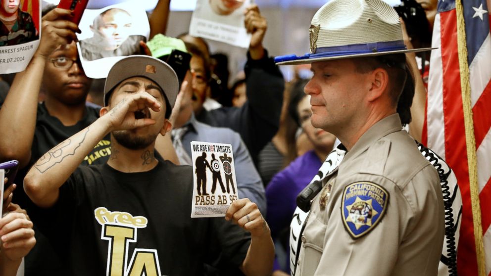 FILE - In this Sept. 2, 2015 file photo, California Highway Patrol Officer J. Nelson stands outside the governor's office as protestors shouting "black lives matter" block the hallway while successfully demanding the passage of AB953, in Sacramento, 