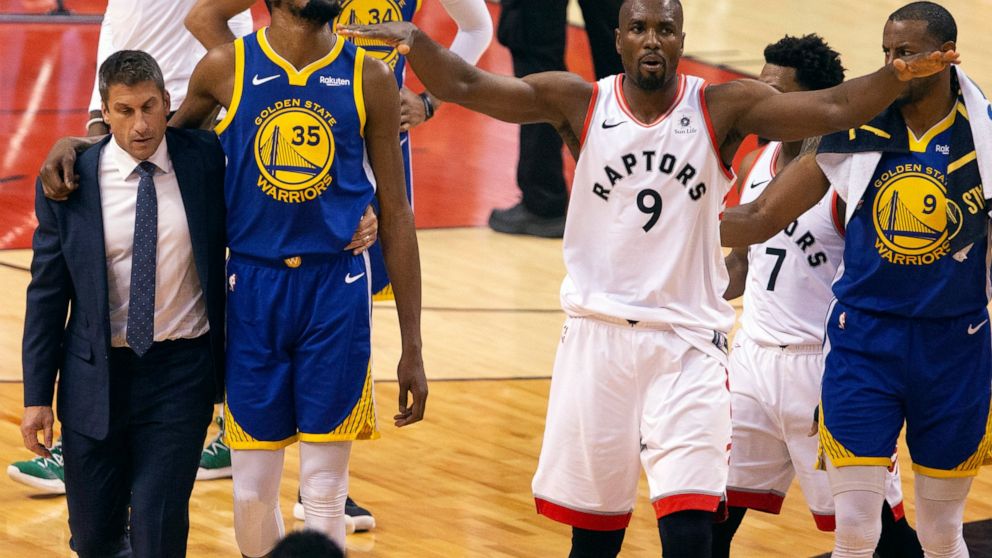 Golden State Warriors forward Kevin Durant (35) walks off the court after sustaining an injury as Toronto Raptors center Serge Ibaka (9) gestures to the crowd during first half basketball action in Game 5 of the NBA Finals in Toronto on Monday, June 