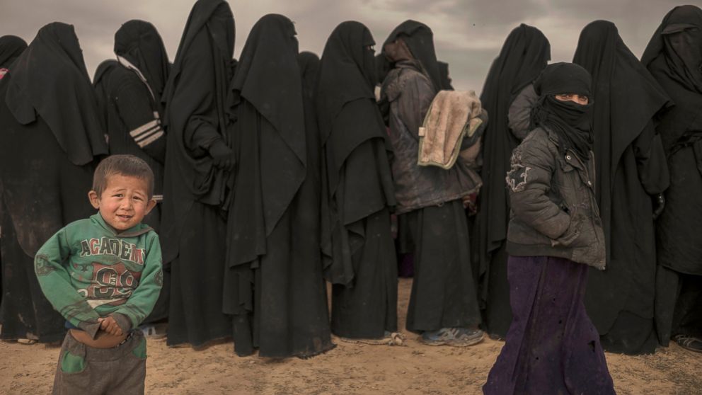 In this Wednesday, March 6, 2019, photo, women and children stand in line at a reception area for people evacuated from the last shred of territory held by Islamic State militants, outside Baghouz, Syria. (AP Photo/Gabriel Chaim)