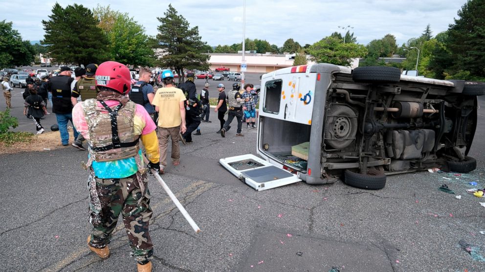 A van that was driven by anti-fascist protesters is pictured flipped on its side with all windows smashed after it was attacked for trying to drive into a Proud Boys rally Sunday, Aug. 22, 2021, in Portland, Ore. (AP Photo/Alex Milan Tracy)