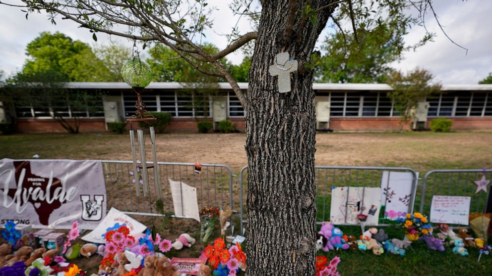 FILE - A cross hangs on a tree at Robb Elementary School on June 3, 2022, in Uvalde, Texas, where a memorial has been created to honor the victims killed in the recent school shooting. Two teachers and 19 students were killed. As public pressure moun