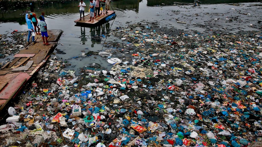 FILE - In this Sunday, Oct. 2, 2016 file photo, a man guides a raft through a polluted canal littered with plastic bags and other garbage in Mumbai, India. United Nations officials say nearly all of the world's countries have agreed on a deal to bett