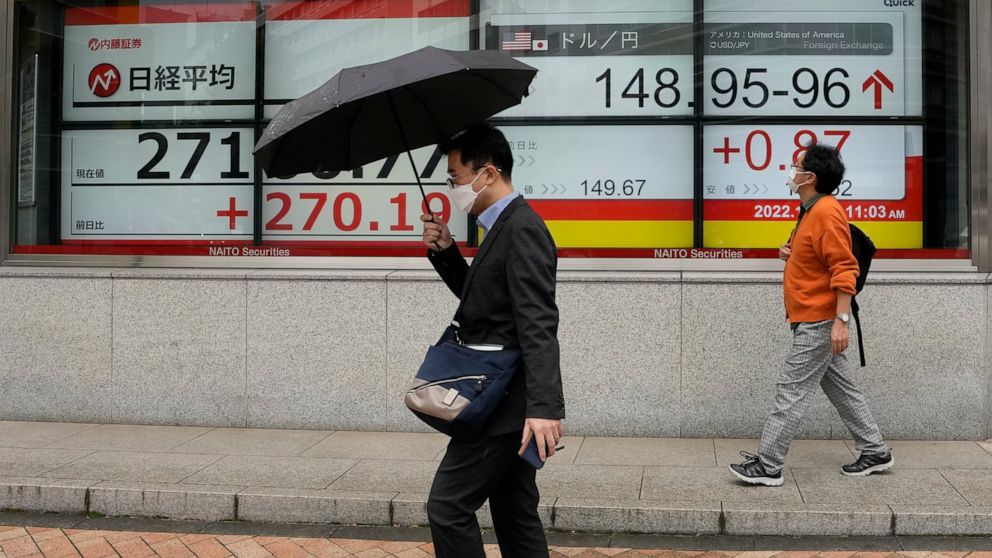 People walk by monitors showing Japan's Nikkei 225 index, left, and the Japanese yen's exchange rate against the U.S. dollar at a securities firm in Tokyo, Monday, Oct. 24, 2022. Hobbled by high interest rates, punishing inflation and Russia's war ag