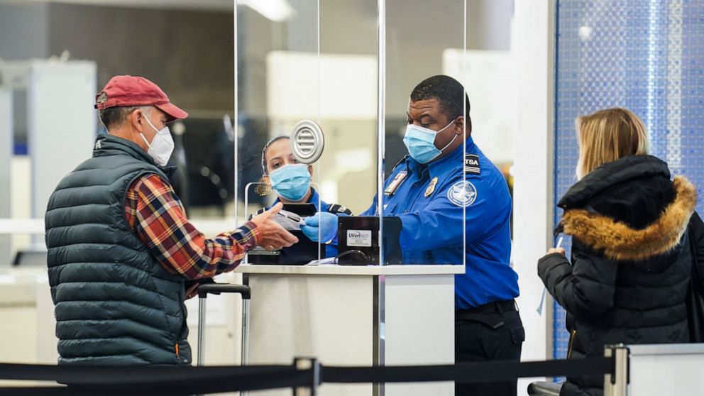 FILE - A Transportation Security Administration agent serves a traveler at a checkpoint in a sparsely populated Terminal B at LaGuardia Airport, Nov. 25, 2020, in the Queens borough of New York. Airlines are canceling more than 1,400 flights across t
