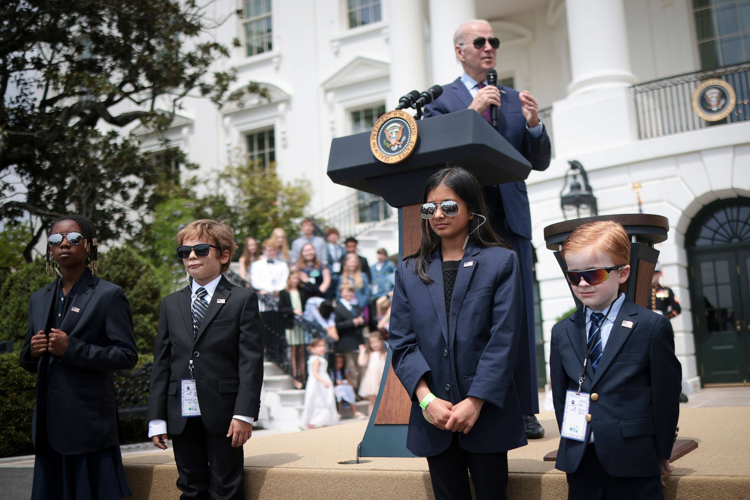 PHOTO: President Joe Biden speaks while children dressed as Secret Service agents "guard" the stage on Take Your Child To Work Day, April 27, 2023, at the White House.