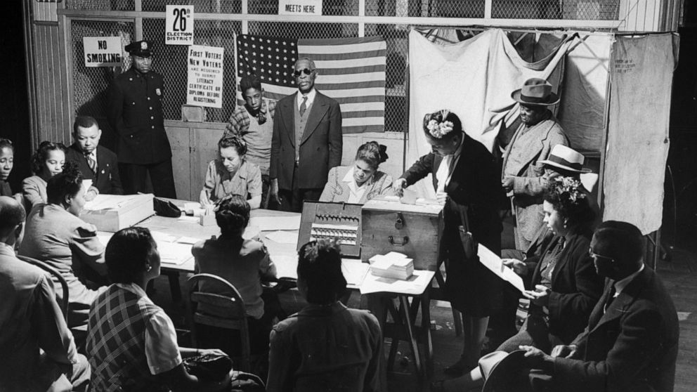 PHOTO: An African-American voter places a paper ballot into a steel box on a table manned by voter registration workers while a police officer stands guard on election day at Public School building in Harlem, New York, circa 1944.