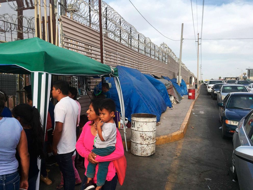 PHOTO: Migrants walk between tents, left, and cars waiting to cross the border between Mexico, and Arizona, May 5, 2019. The tent slots are for families about to be called, allowing them to be ready on a moment's notice. 