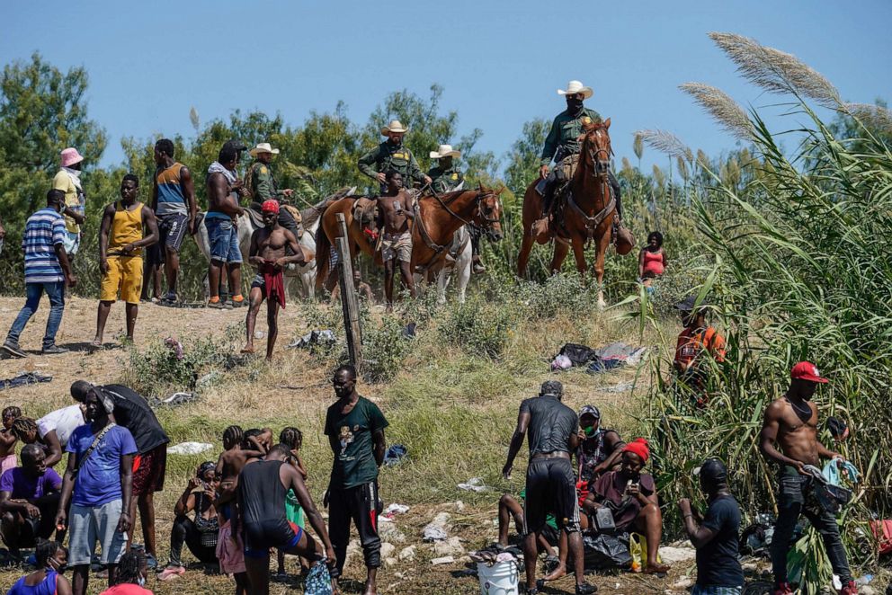 PHOTO: U.S. Border Patrol agents on horseback look on as Haitian migrants sit on the river bank near an encampment on the banks of the Rio Grande near the Acuna Del Rio International Bridge in Del Rio, Texas on Sept. 19, 2021.