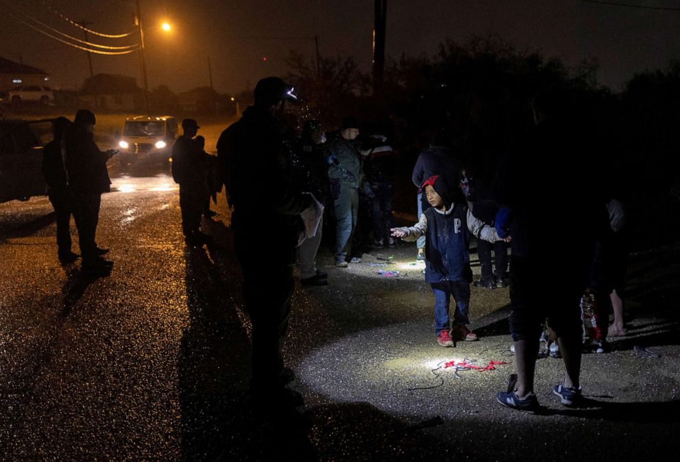 PHOTO: A migrant boy attempts to catch raindrops, backlit by a border patrol agent's headlamp, as he and his family await to be registered after being smuggled across the Rio Grande river from Mexico into Roma, Texas, Nov. 18, 2022.