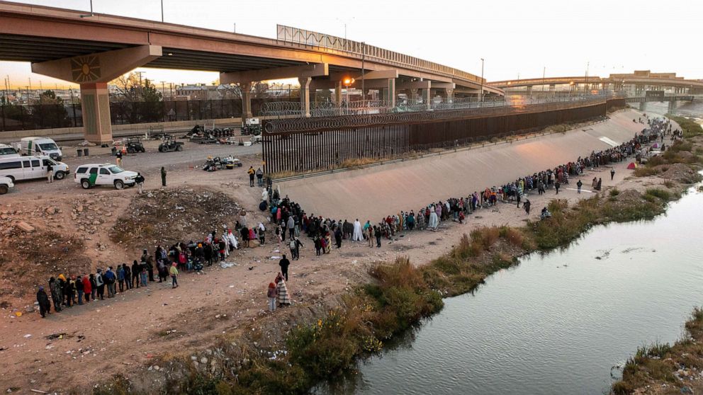 FOTO: Migrantes hacen fila cerca del muro fronterizo después de cruzar el río Bravo para entregarse a los agentes de la Patrulla Fronteriza de EE. UU. que buscan asilo en la ciudad estadounidense de El Paso, Texas, visto desde Ciudad Juárez, en México, el 12 de diciembre de 2022.