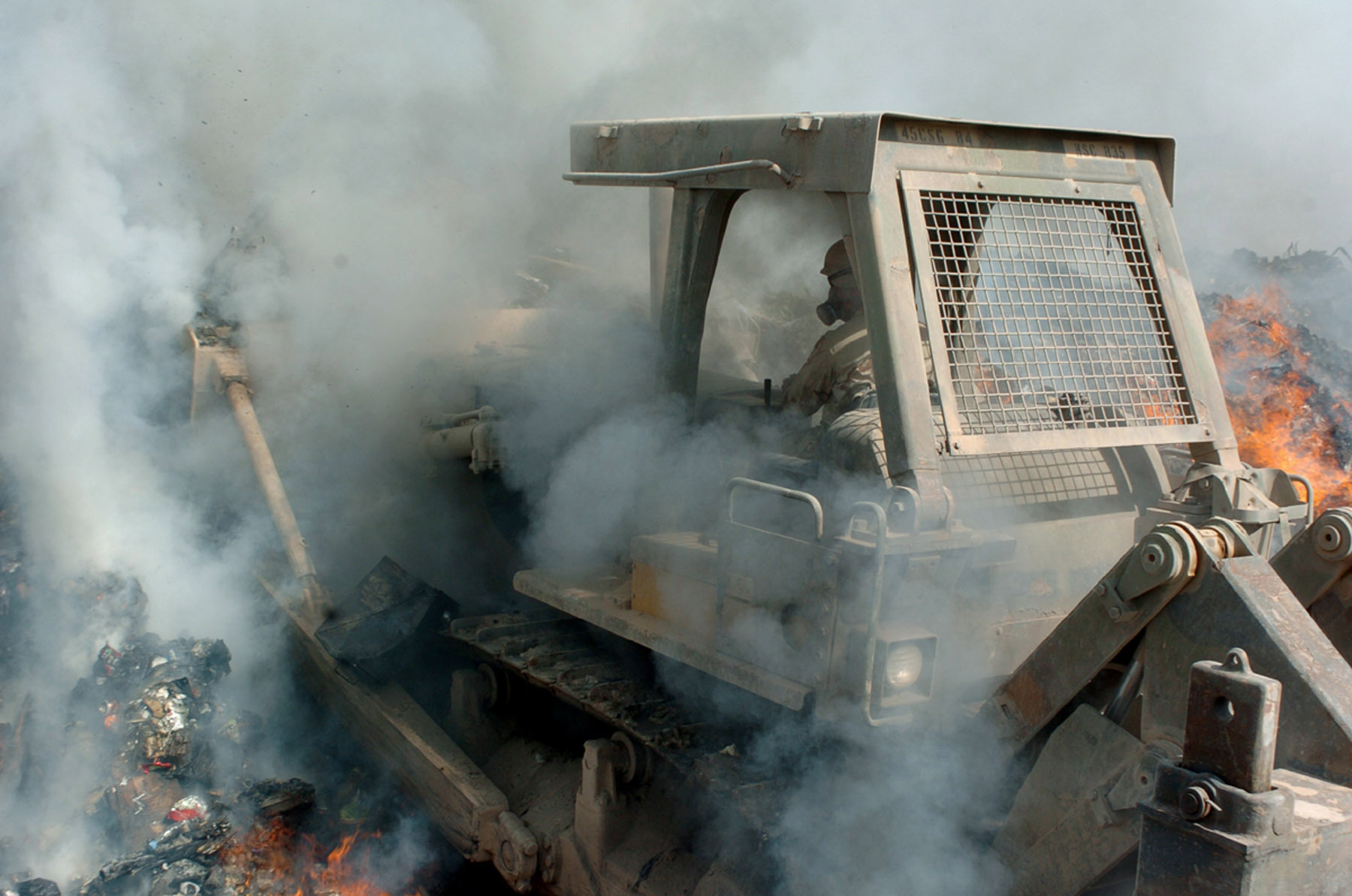 PHOTO: Smoke billows in from all sides as a member of the U.S. military pushes a bulldozer deep into the flames of a burn pit to keep burnable items constantly ablaze, at Balad Air Base in Iraq, Sept. 24, 2004.