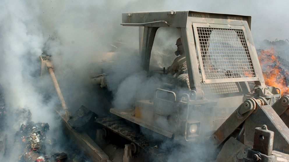 PHOTO: Smoke billows in from all sides as a member of the U.S. military pushes a bulldozer deep into the flames of a burn pit to keep burnable items constantly ablaze, at Balad Air Base in Iraq, Sept. 24, 2004.