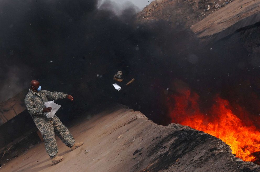 PHOTO: A member of the 332nd Expeditionary Logistics Readiness Squadron tosses unserviceable uniform items into a burn pit at Balad Air Base in Iraq, March 10, 2008.