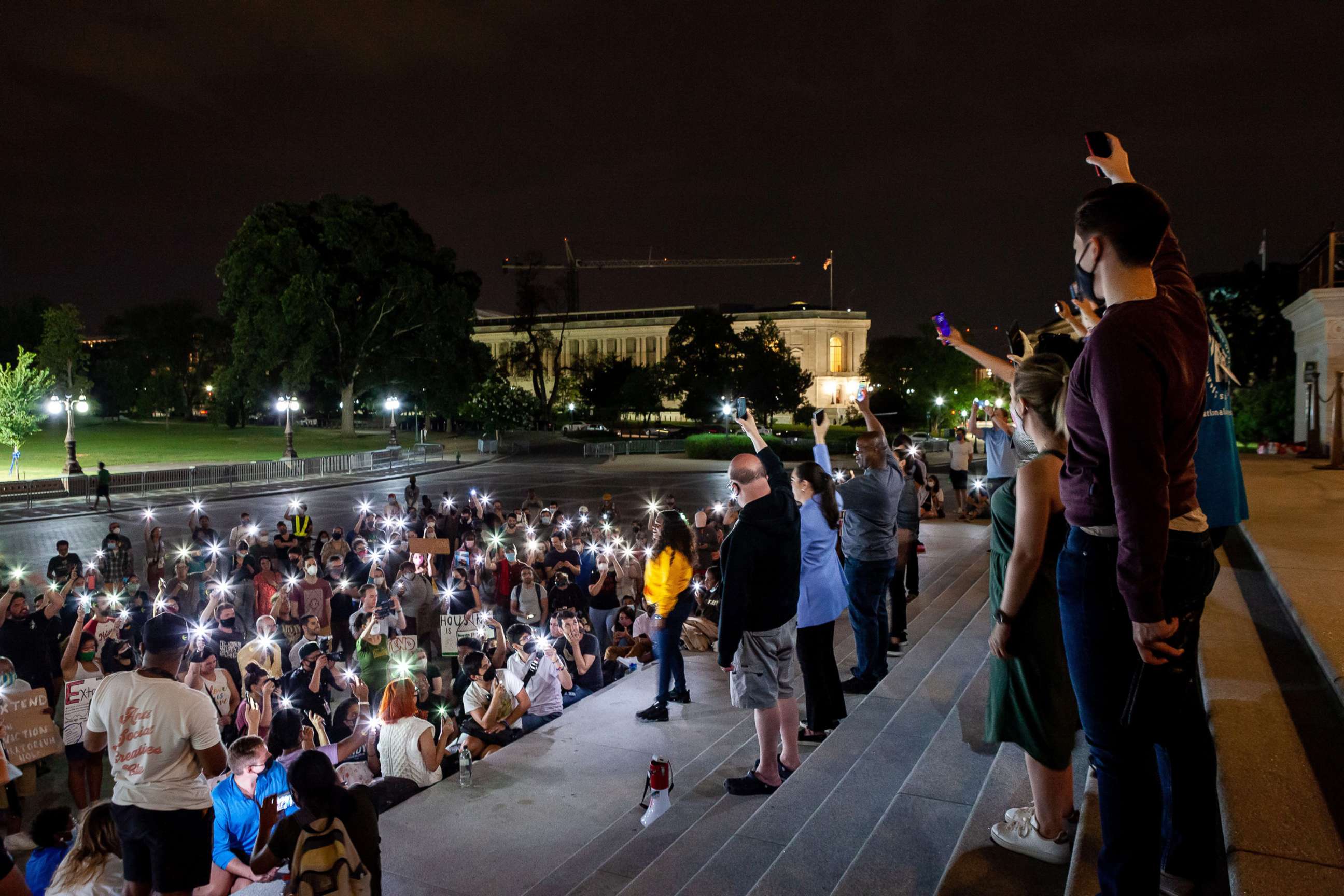 PHOTO: Protesters at a midnight rally on the steps of the Capitol hold their phones in the air with Congresswoman Cori Bush, in yellow, in a moment of silence to remember those who have been lost due to homelessness and the pandemic.
