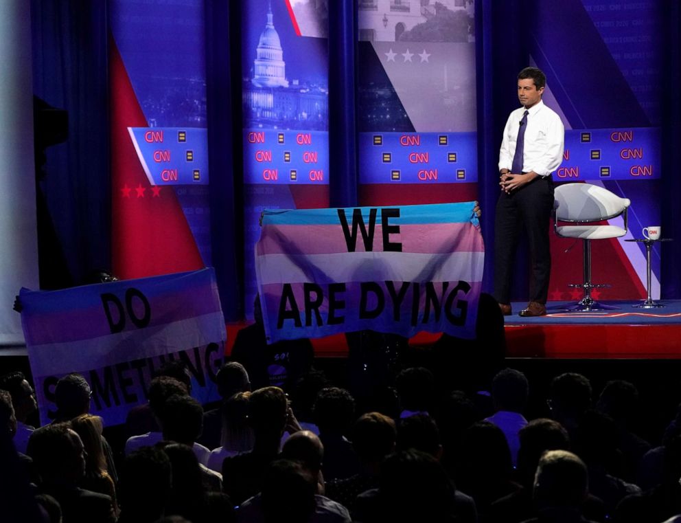 PHOTO: Democratic 2020 U.S. presidential candidate South Bend, Indiana, Mayor Pete Buttigieg looks on as protesters hold a banner in a televised town hall on CNN dedicated to LGBTQ issues in Los Angeles on Oct. 10, 2019. 