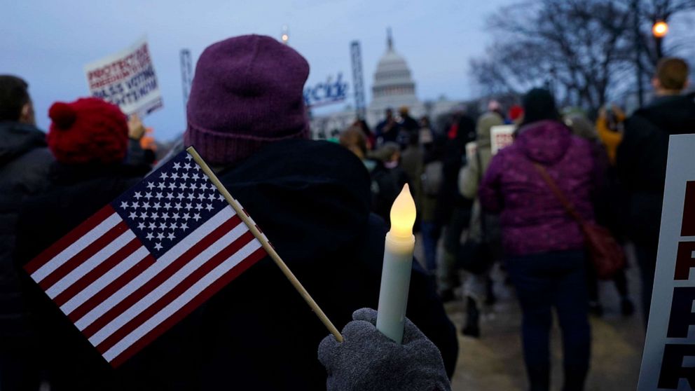 PHOTO: With the Capitol building in the background, a person holds an American flag and a flameless candle during a vigil, Jan. 6, 2022, in Washington, D.C., on the one year anniversary of the attack on the Capitol.