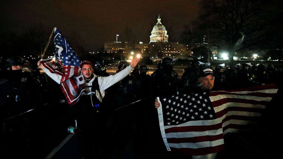 PHOTO: Supporters of President Donald Trump hold U.S. flags as they walk next to police near the Capitol during a protest against the certification of the 2020 U.S. presidential election results by the congress, Jan. 6, 2021.